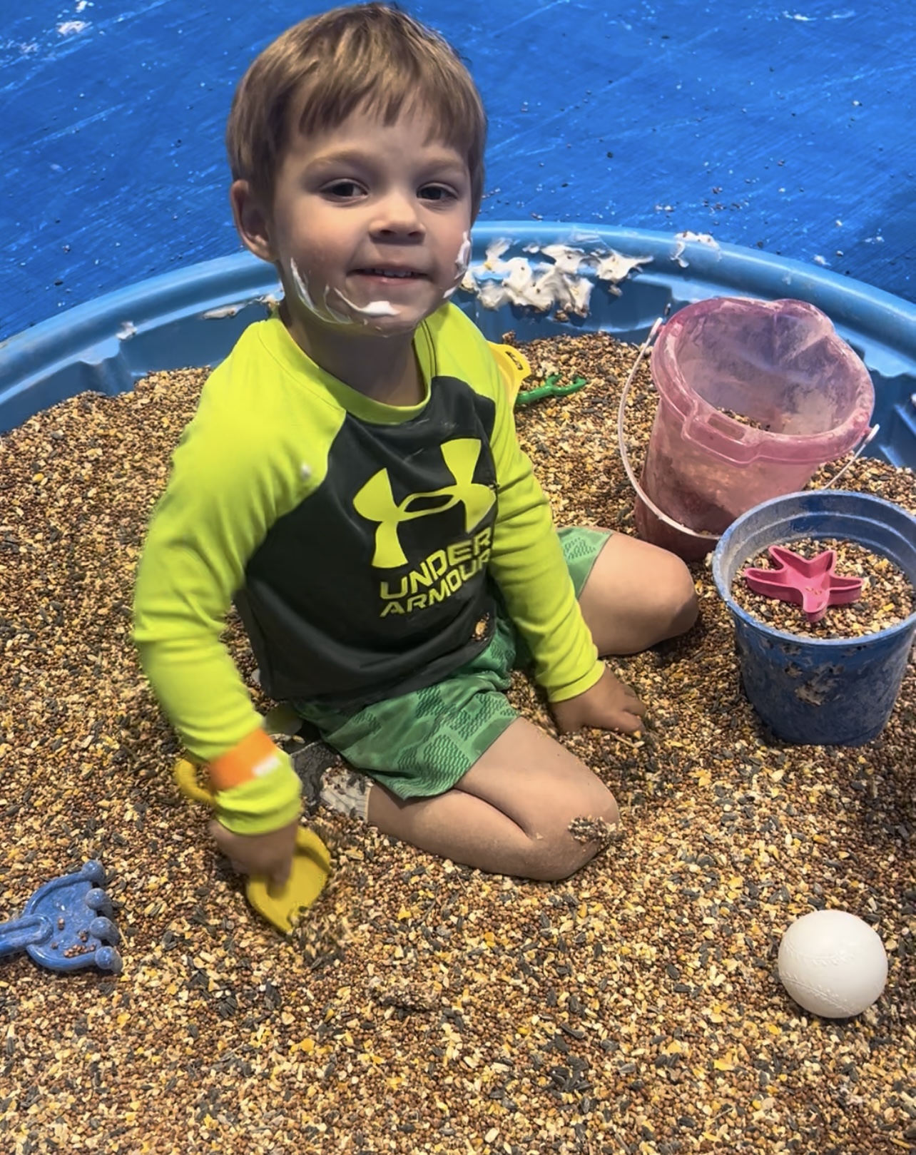 Smiling kid in a bucket surrounded by toys.